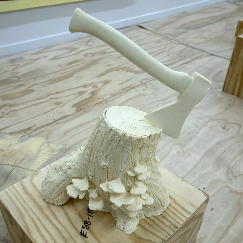 A butter yellow tree stump with an axe in it and shelf mushrooms on the side on top of a plywood box.