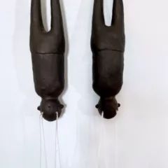 Two human figures in brown stoneware clay hang upside down. They are missing their arms and tears in the form of white twine fall out of their eyes.