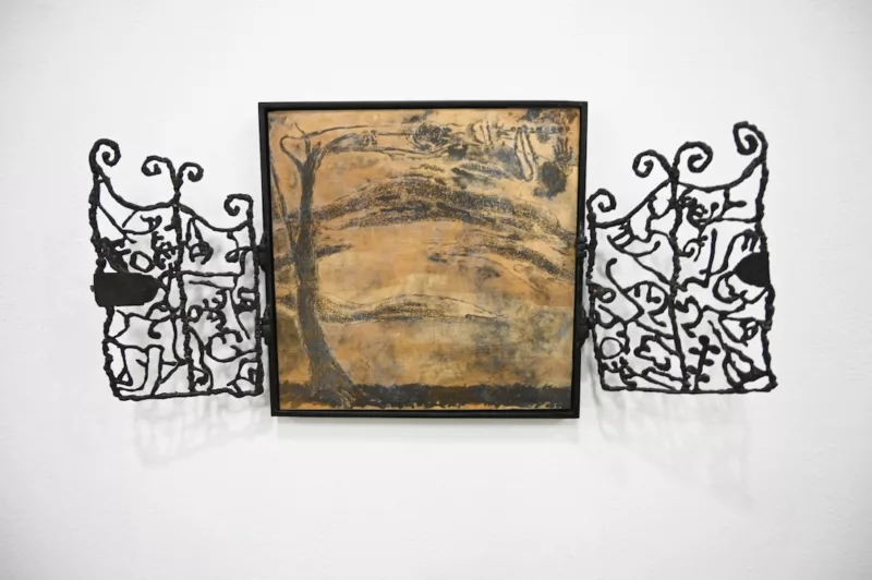 A framed painting of a dark forbidding landscape is bracketed by ornamental gate-like panels on left and right sides. 