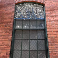 A window at the Crane Arts building with plastic wrapped electrical wires weaved into the grating of the window. The dominant color is white with a branched tree pattern of blue lining the bottom.