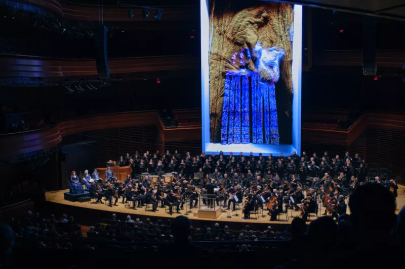 Philadelphia Orchestra playing beneath an Ai generated image by artist Refik Anadolit showing an image of an almost ultaviolet blue church window and a brown amorphous form of textile like quality.