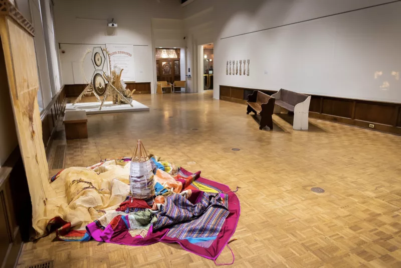 A gallery with a parquet floor shows a group of objects in a four-person show, “Songs of Ritual and Remembrance,” in which personal experience of migration from war-torn country, slavery, and workers’ rights struggles are encapsulated in widely different media, from wall works, to large sculptural installations.