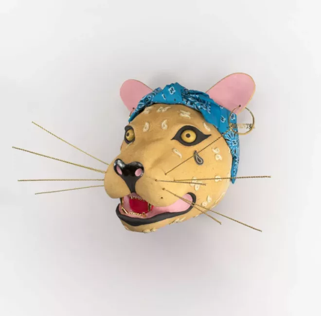 A jaguar head on a wall with a paisley bandana and hoop earring with a name inside. The pattern of the jaguar is replaced with the teardrop shape featured in bandanas. The teeth of the Jaguar are gold as if a grill. Long straight coils of yellow come out as the whiskers.