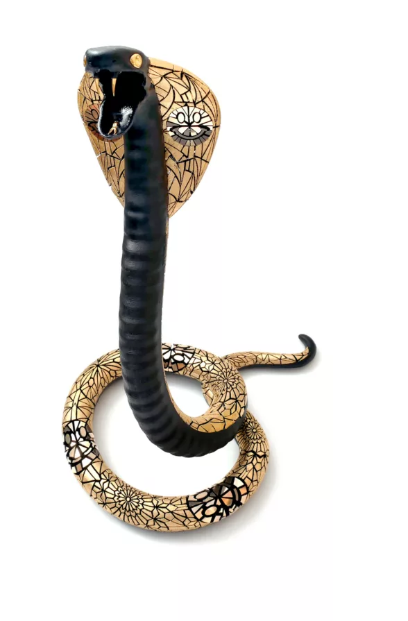An ornate, black-and-gold sculptural figure of a king cobra snake rises up, its mouth open and fangs threatening. The piece’s bejeweled affect suggests it is a symbol of status for a person of high rank. The piece was 3-D printed and then embellished with gold leaf.