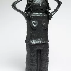 A black ceramic figure of a woman with her thin hands on her head and a sad or shocked face.