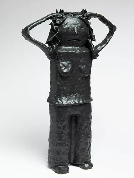 A black ceramic figure of a woman with her thin hands on her head and a sad or shocked face.