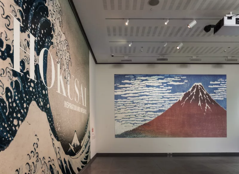 Installation view of Hokusai at MFA Boston. Shows the great wave off kanagawa to the left and a work depicting a mountiain on the back wall.
