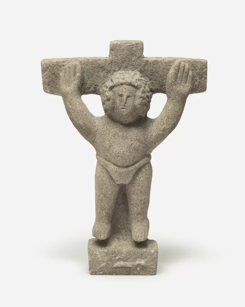 A limestone sculpture by William Edmondson of Jesus Christ on the crucifix. Jesus appears in a loincloth with arms raised and legs spread. No stigmata appear on his appendages and no signs of pain are visible instead a placid look stares back at the viewer.
