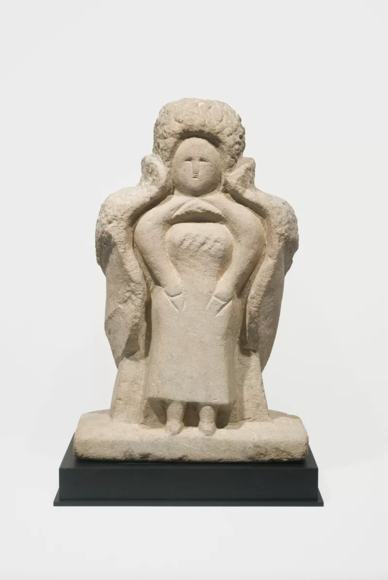 Limestone sculpture of Eleanor Roosevelt by William Edmondson. The form of Eleanor appears out of the block with a slight squinted eye feature and minimal expression. Her arms lay on her pelvis. A overcoat appears out of the stone and envelopes the back of her form.