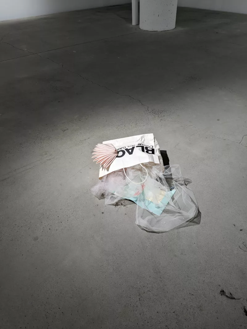 A shopping bag on the floor of a gallery spilling gout it's contents.