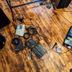 A photo shows a wood gallery floor with many electronic devices connected together with long black and some white cables. Part of a show about technology today.