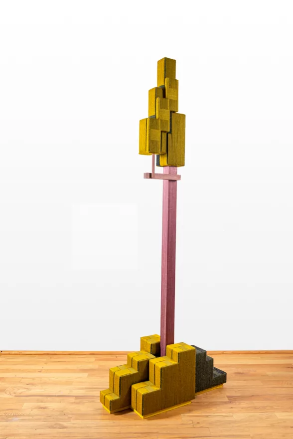 A sculptural piece, blocky with “feet” at the bottom, a pole jutting up from the “feet” and ending in more blocks at the top and what looks like one arm bent up at the elbow giving support to the top stack of blocks