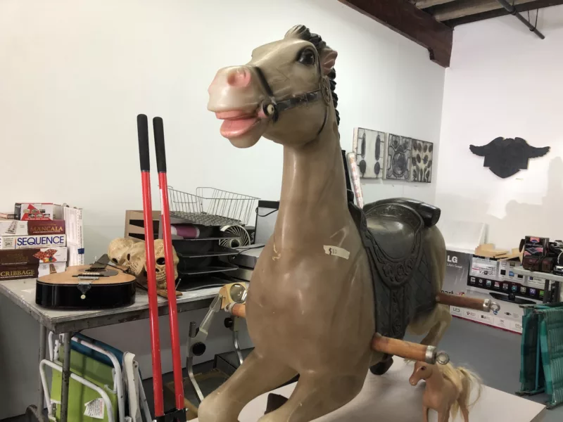 Tables filled with “stuff,” like a guitar, some board games, a carousel horse, folding chairs and more, all for sale after a gallery closed its doors.