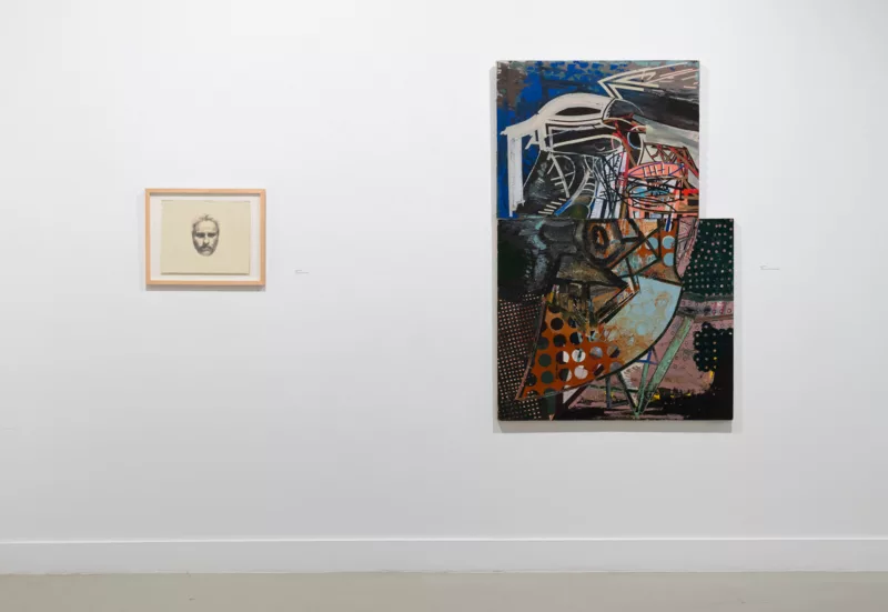 Two images on a white gallery wall represent self-portraits of the artist, David Kettner, done ten years apart, with the earlier being a figurative likeness of a face and the later being a designed, abstract, geometric display.