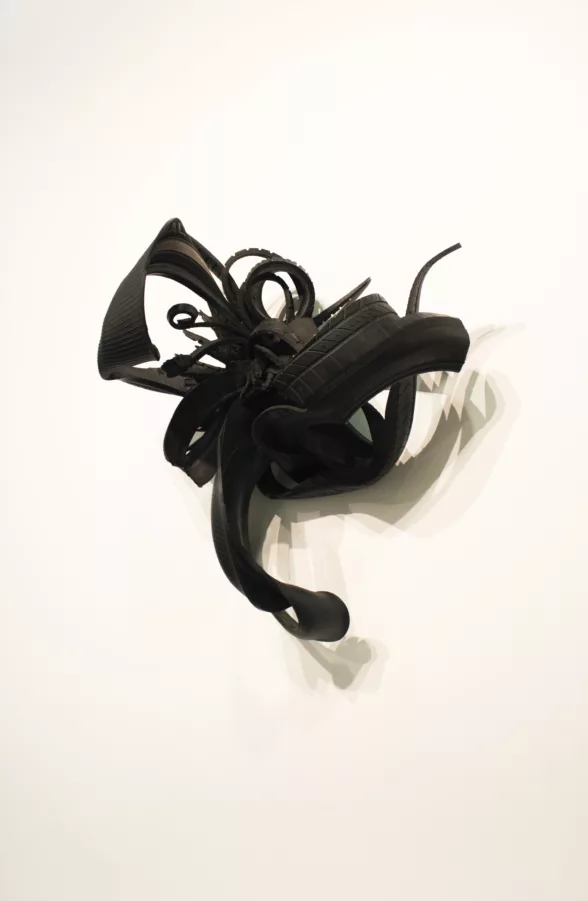 A black sculpture by Chakaia Booker on a white wall with sumptuous curves and facets suggests a beautiful object of desire, however close inspection shows is is made of rubber car tires.