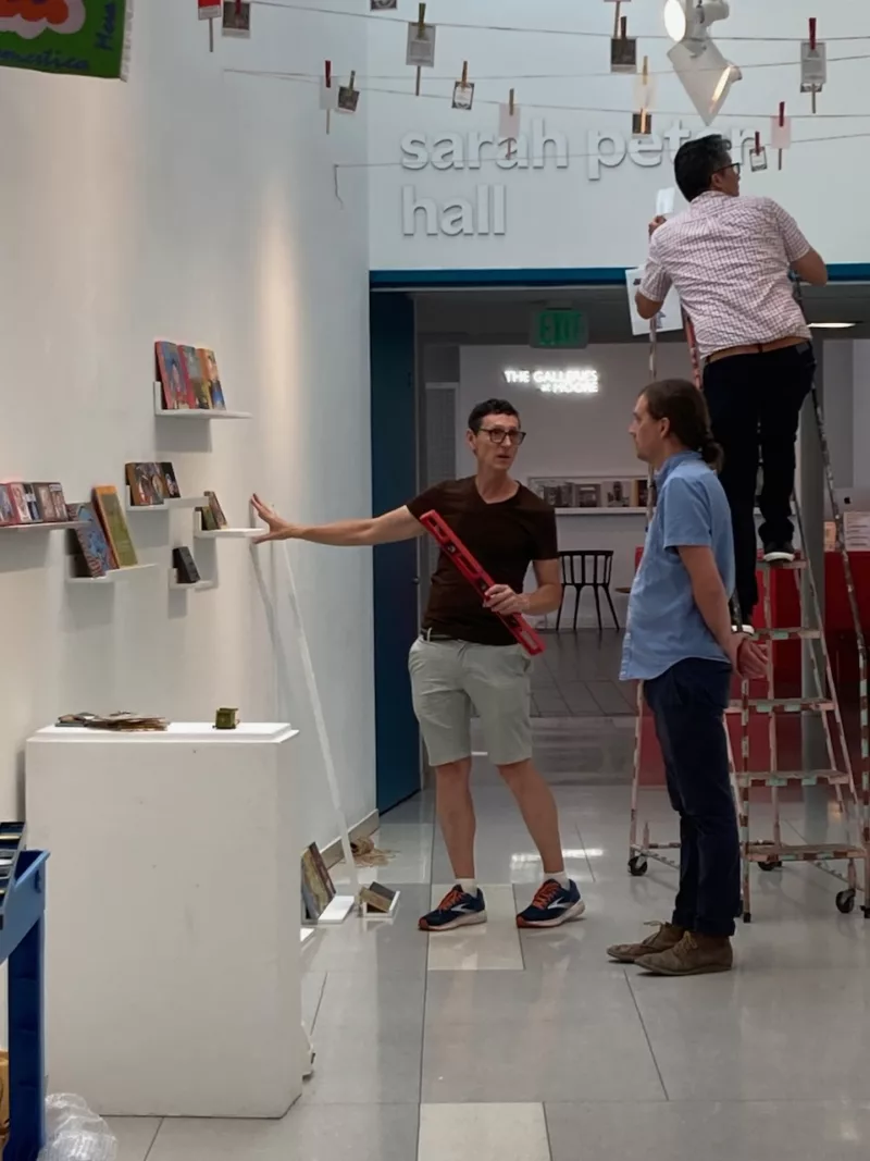 People installing art in a hallway for an art exhibit.