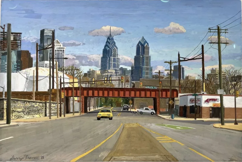 We are looking down a broad, mostly empty boulevard. A few hundred feet ahead is a train trestle crossing the roadway. Beyond the trestle, in the distance we see the tops of Philadelphia skyscrapers. 