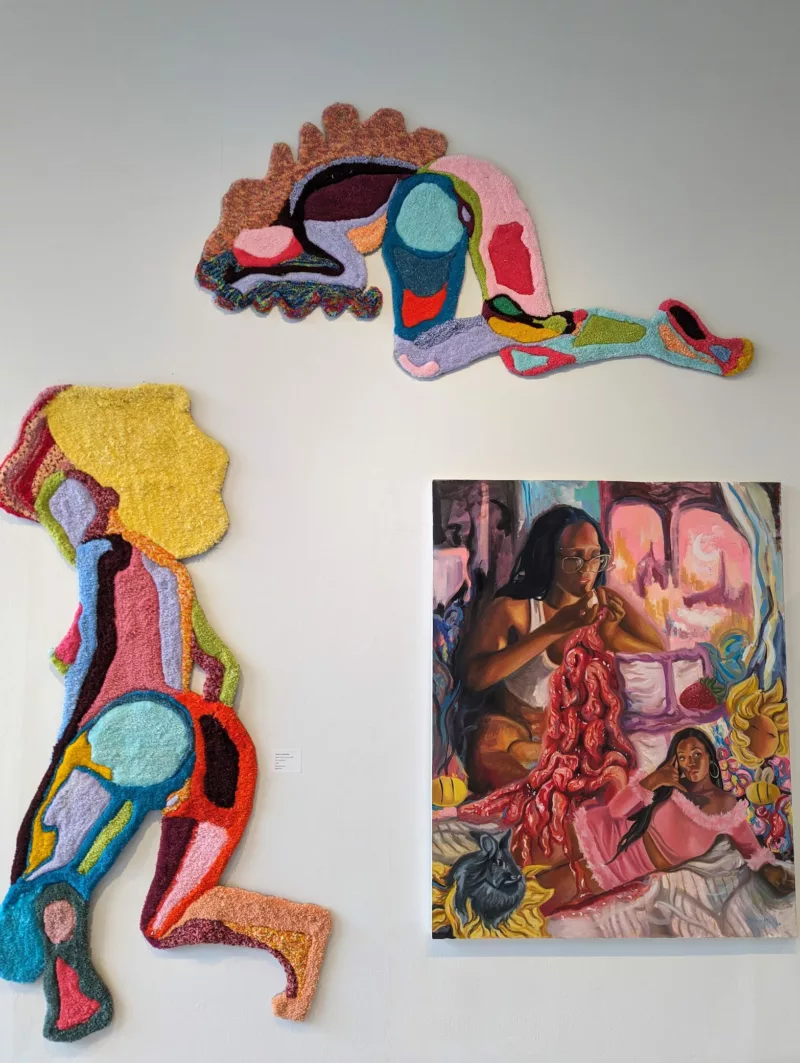 Three colorful textured works on a white wall in an art exhibit show images of women in stages of distress and self harm. 
