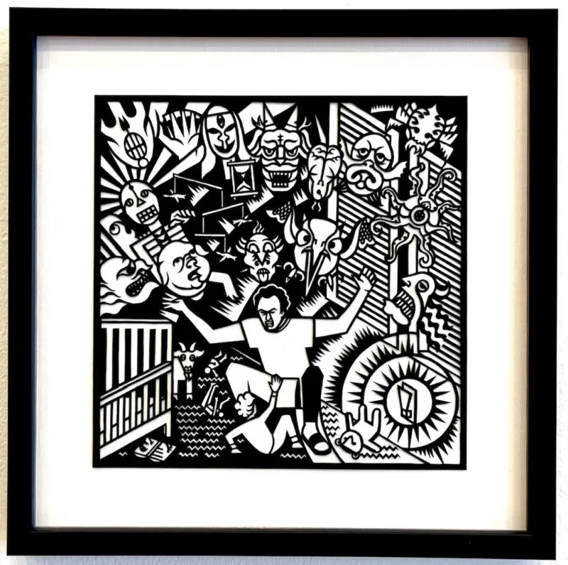 In this small, square black and white paper cut out, a father kneels over a small child at the bottom center of the picture. The father’s hands are outstretched, and behind him, filling the upper two thirds of the picture, are many demon masks.