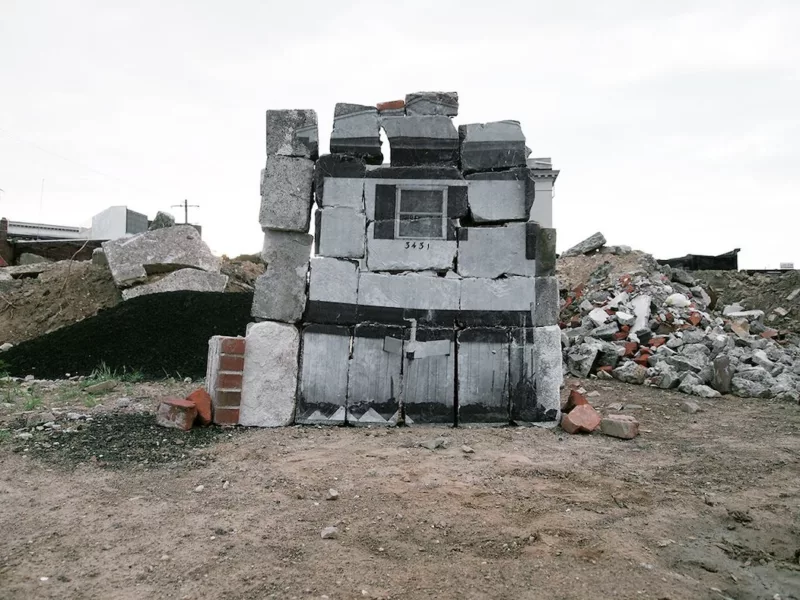 A sculpture created from cinder blocks and used concrete blocks is meant to look like a mobile home. There’s a window and a house number under it in the middle.