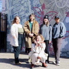 A group of five people, standing in bright sunlight, dressed in winter clothes, stand on the side of DVAA’s building.