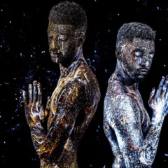 Two Black male figures in a black cosmic background stand back to back, their hands clasped in prayer their eyes cast down with what looks like tears cascading down their faces.