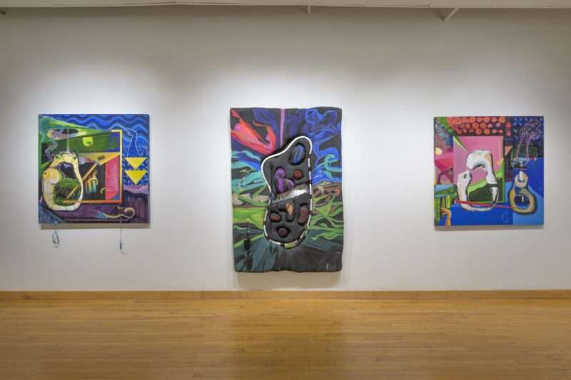 Three large, bright-colored paintings sit on a white wall above a light wood floor, their subjects seem to refer to body parts and allude to science and healing.