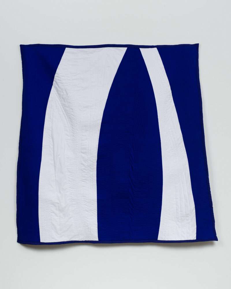 A large square quilted cotton cloth wall hanging shows two bright white strips of fabric curving upwards and almost meeting at the top, surrounded by a deep navy blue background. 