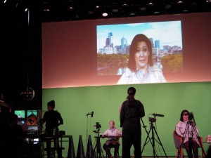 Audrey Crabtree, seated, right, and projected on the top video screen, presented an Oprah- or Diane Sawyer-like persona, poker-faced and empathetic -- but manipulative.