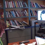 Library with woman looking at tv screen with woman's image on screen.